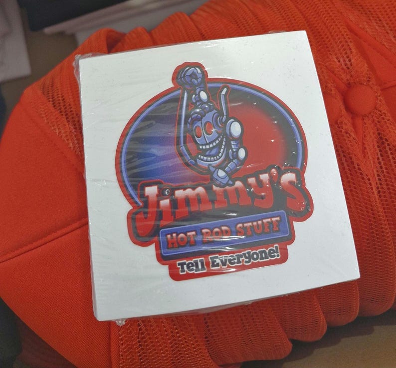 May include: White sticker with a red, blue, and black logo for Jimmy's Hot Rod Stuff. The logo features a cartoon robot holding a wrench and the text "Tell Everyone!"