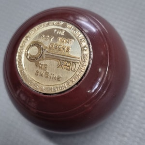 May include: A dark red bowling ball with a gold emblem that reads "The Key That Opens The Engine X490" and "Superior Circle Piston Expanders".