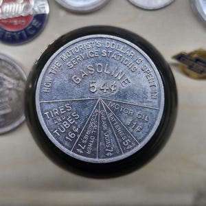 May include: A round black object with a silver metal top featuring a pie chart graphic titled How the Motorist's Dollar is Spent in Service Stations. The chart lists Gasoline 54 cents, Motor Oil 11 cents, Batteries 5 cents, Grease Jobs 7 cents, All Other Accessories 7 cents, and Tires and Tubes 16 cents.