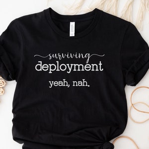 May include: Black t-shirt with white text that reads "surviving deployment yeah, nah."