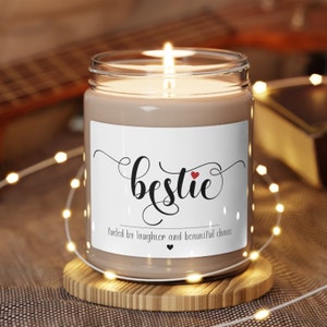 May include: A brown candle in a clear glass jar with a white label that says "bestie" with a red heart and the text "Fueled by laughter and beautiful chaos".