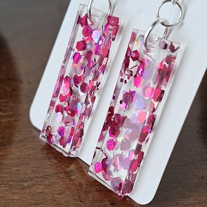 May include: A pair of pink glitter rectangle earrings with silver hooks.