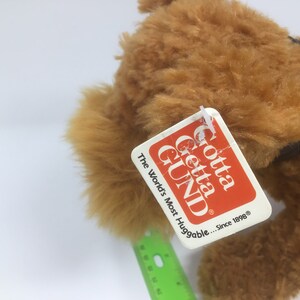 May include: A brown plush dog with a black collar. The dog has a tag that says "Gotta Getta GUND" and "The World's Most Huggable... Since 1898".