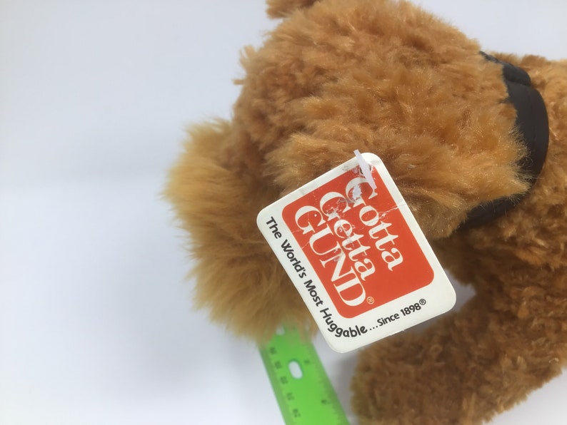 May include: A brown plush dog with a black collar. The dog has a tag that says "Gotta Getta GUND" and "The World's Most Huggable... Since 1898".