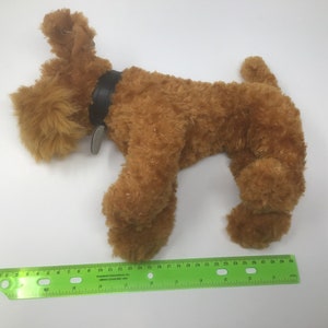 May include: A brown plush toy dog with a black leather collar and a tag. The dog is lying on its side with its head turned to the left. The dog is about 12 inches long.