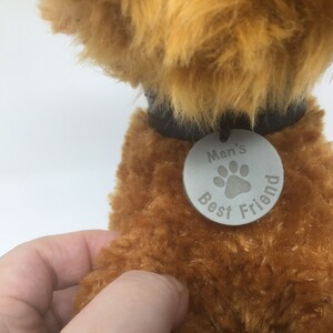 May include: A brown plush toy dog wearing a black collar with a silver tag that reads "Man's Best Friend" with a paw print.