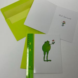 Cartão de felicitações com sapo fofo e flor, dentro de um bilhete "só porque sim" com vaso de flores, envelope verde combinando