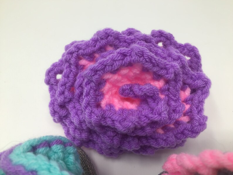 K&ouml;nnte beinhalten: Eine lila geh&auml;kelte Blume mit einem rosa Zentrum. Die Blume ist aus weichem, strukturiertem Garn gefertigt.