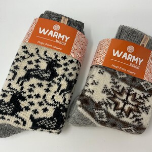 May include: Two pairs of warm wool socks with different patterns. The socks are grey with white and black designs. The socks have a label that says "Warmy Brand, Hugs from nature".