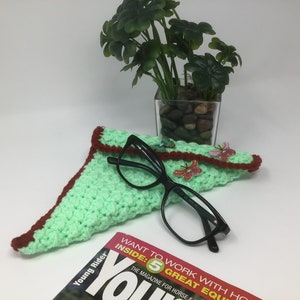 May include: A green crocheted eyeglass case with a red border. The case is decorated with small butterfly embellishments. A pair of black eyeglasses is resting on top of the case. The case is lying on a magazine with the text "Young Rider" and "Want to work with horses inside: 5 great equipment" visible.
