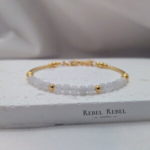 Puede incluir: Un delicado brazalete con cuentas de piedras preciosas blancas y detalles dorados. El brazalete está hecho con un diseño simple y es perfecto para el uso diario.