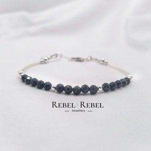 May include: A delicate silver bracelet with black gemstone beads. The bracelet features a simple design with alternating silver and black beads. The bracelet is perfect for everyday wear.