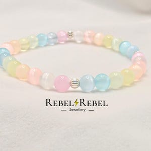 Peut inclure: Un bracelet en perles de couleur arc-en-ciel pastel avec des accents argentés. Le bracelet est composé de petites perles rondes dans des tons de rose, bleu, jaune et blanc.
