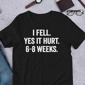 Könnte beinhalten: Schwarzes T-Shirt mit weißem Text, der "I fell. Yes it hurt. 6-8 weeks." lautet.