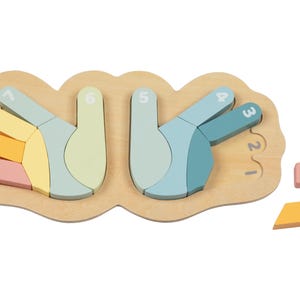 May include: A wooden puzzle shaped like two hands with numbers 1-10 on each finger. The puzzle pieces are in pastel colors and are missing from the puzzle. The puzzle pieces are on a white background.