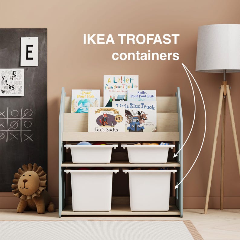 May include: A white wooden bookshelf with blue accents and four white storage bins. The bookshelf is filled with children's books with colorful covers. The text on the bookshelf reads "IKEA TROFAST containers".