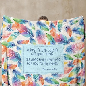 May include: A colorful feather-patterned blanket with text that reads, "a best friend doesn't clip your wings... She adds more feathers for you to fly higher! Love you bestie!" The feathers are in shades of blue, orange, green, and purple.