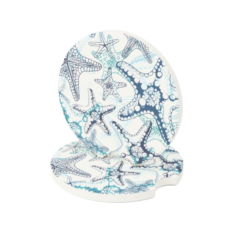 Pu&ograve; includere: Due sottobicchieri in ceramica bianca con un motivo a stelle marine blu e turchese. I sottobicchieri sono rotondi con un bordo a festoni.