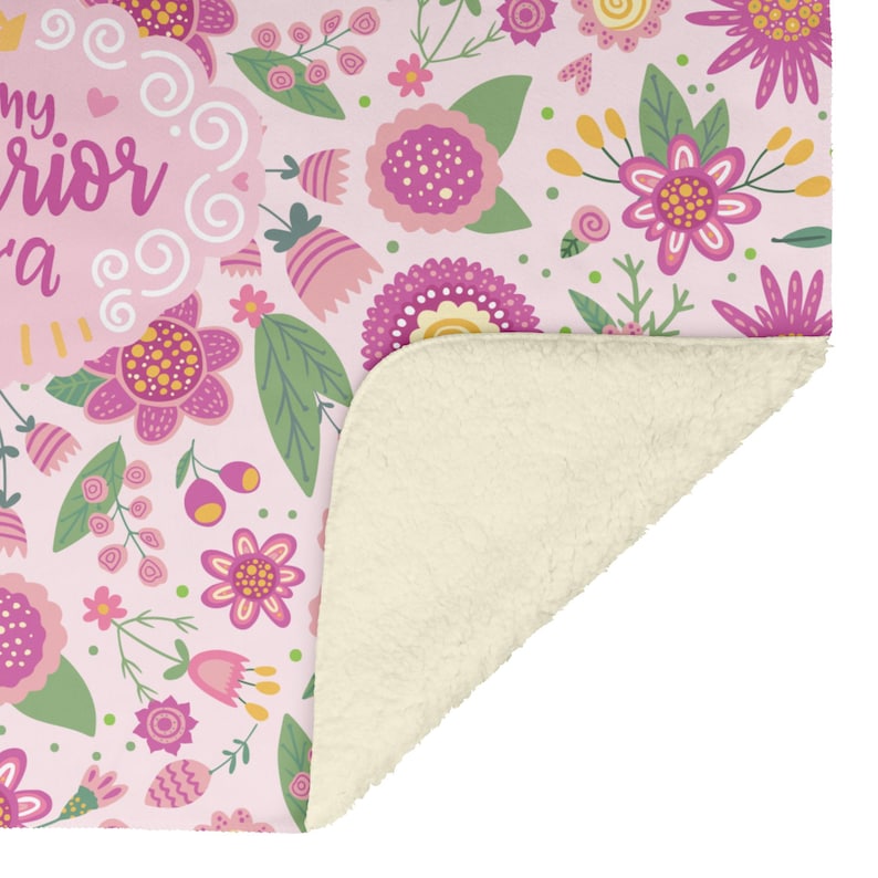 K&ouml;nnte beinhalten: Rosa Decke mit Blumenmuster und cremefarbenem Sherpa-Futter. Die Decke zeigt ein sich wiederholendes Muster aus stilisierten rosa und lila Blumen mit gr&uuml;nen Bl&auml;ttern. Der Text "my warrior" ist auf der Decke zu sehen.