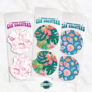 Pu&ograve; includere: Set di sei sottobicchieri per auto con tre diversi design. I design includono conchiglie rosa e bianche, foglie tropicali verdi e rosa e conchiglie blu e rosa. I sottobicchieri sono confezionati in sacchetti di plastica trasparente con la scritta "Summer Brights Car Coasters" stampata su ogni sacchetto.