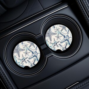 Pu&ograve; includere: Due sottobicchieri rotondi per auto con sfondo bianco e un motivo a stelle marine blu e bianco.