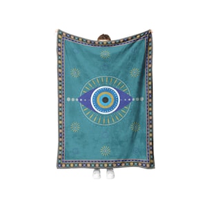 May include: A teal blue throw blanket with a large blue eye design and a gold and white border. The eye has a black pupil and a yellow iris.