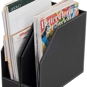 May include: Black leather magazine holder with two compartments. The holder has white stitching and is filled with magazines and notebooks. The magazines have the title "Better Homes & Gardens" and the notebooks have the title "Docket".