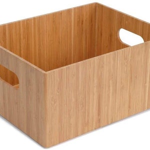 May include: A natural bamboo storage box with two cut-out handles on the sides. The box has a wood grain pattern and a small logo on the bottom right corner that reads "WoodWick."