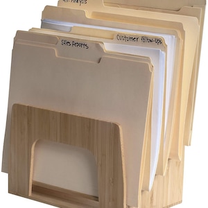 Puede incluir: Un organizador de archivos de bamb&uacute; que contiene varias carpetas de archivos de Manila. Las carpetas est&aacute;n etiquetadas con un marcador negro, incluyendo "Qtr. Analysis", "Sales Reports" y "Customer Follow-ups". El organizador tiene un acabado de madera natural.