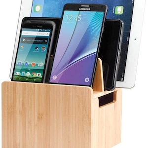 May include: A bamboo charging station with slots for three phones and a tablet. The station has a black interior and a natural wood finish.