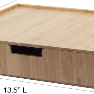 Może przedstawiać: Bambusowy organizer biurkowy z szufladą. Organizer ma 34,3 cm długości, 24,1 cm szerokości i 7,6 cm wysokości. Szuflada ma wycięty uchwyt. Bambus ma jasnobrązowy kolor.