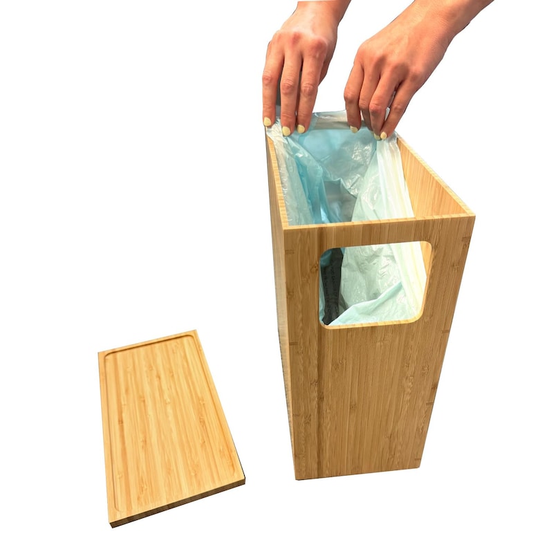 May include: A bamboo trash can with a removable lid and a built-in liner holder. The can is made of natural bamboo and has a light brown color. A blue plastic trash bag is partially inserted into the can.
