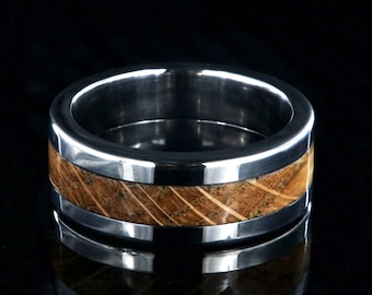 Puede incluir: Un anillo de plata con una incrustación de madera marrón. La madera tiene un patrón rayado.
