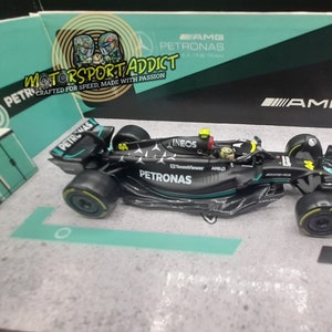 May include: A black and green 1:18 scale model of a Formula 1 race car. The car has the logos of Petronas, Ineos, and AMG. The car is on a display stand.