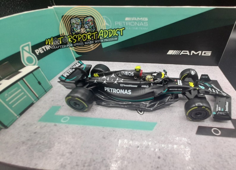 May include: A black and green 1:18 scale model of a Formula 1 race car. The car has the logos of Petronas, Ineos, and AMG. The car is on a display stand.