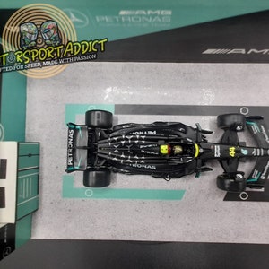 May include: A black and green Formula 1 race car model with the number 44 on the side. The car is on a display stand with the Petronas logo and the words "Motorsport Addict" and "Grafted for speed, made with passion".