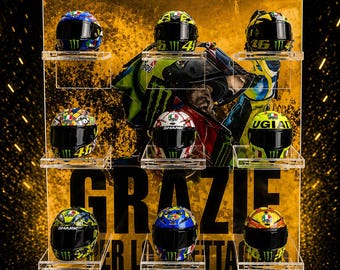May include: A clear acrylic display stand holding nine miniature motorcycle helmets in three rows. The background features a yellow and black graphic with the text MOTORSPORT ADDICT, CRAFTED FOR SPEED. MADE WITH PASSION, and GRAZIE.