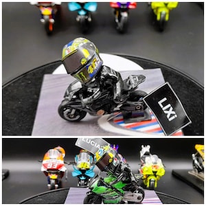 Puede incluir: Dos figuritas de moto en miniatura con pilotos que llevan cascos. La primera figurita es negra y amarilla con el número 46 en el casco. La segunda figurita es verde y negra con el número 46 en el casco. Las figuritas están sobre una superficie a cuadros en blanco y negro con la palabra "LIXI" en un cartel negro.