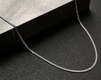 May include: A silver chain necklace on a gray surface. The chain is made of small, linked squares.