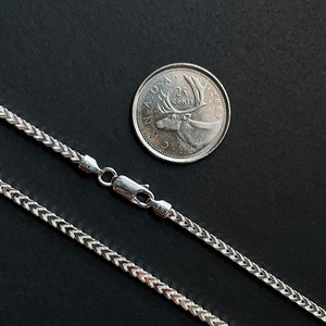 May include: A silver chain necklace with a lobster clasp. The chain is a foxtail design. A Canadian 25 cent coin is included for size reference.