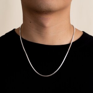 Op de afbeelding: Een zilveren kettingketting gedragen door een persoon die een zwart shirt draagt.