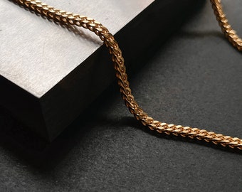 Op de afbeelding: Een gouden ketting met een delicaat, ingewikkeld ontwerp. De ketting is gemaakt van kleine, met elkaar verbonden stukjes die een fijne, delicate uitstraling creëren.