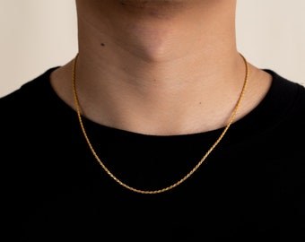 Op de afbeelding: Een gouden touwkettingketting gedragen door een persoon met een zwart shirt.
