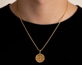 Op de afbeelding: Goudkleurige kompas hanger ketting. De hanger heeft een gedetailleerd kompasontwerp. De ketting heeft een touwketting en wordt getoond tegen een zwarte achtergrond.