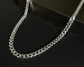 Op de afbeelding: Een zilveren gourmetketting die op een zwart oppervlak wordt getoond. De ketting is gemaakt van in elkaar grijpende schakels die licht reflecteren. De ketting is een eenvoudig, maar elegant sieraad.