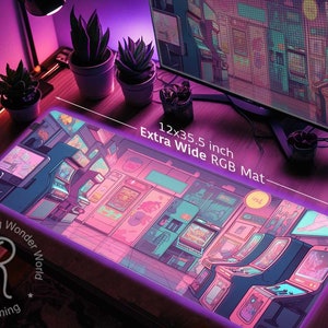 May include: An extra-wide RGB gaming mat, 12 x 35.5 inches, featuring a vibrant arcade game design in pink, purple, and blue hues. The mat has a neon-like border and includes the text "Extra Wide RGB Mat".
