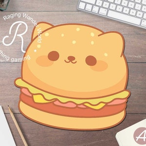 以下が含まれることがあります： 白い輪郭のある黄色とオレンジの猫の形をしたハンバーガーのコンピューターマウスパッド。マウスパッドはゴマの入ったバンズ、ピンクのハンバーグ、黄色のチーズが付いています。猫は大きく可愛い目と小さな鼻をしています。