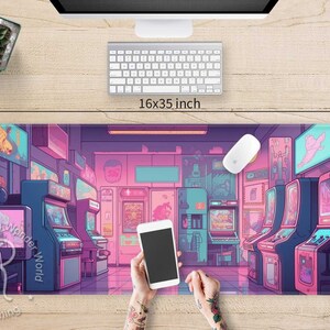 May include: A rectangular gaming mouse pad with an arcade game scene in shades of pink, purple, and blue. The pad measures 16x35 inches. A computer mouse, keyboard, and a smartphone are on the pad.