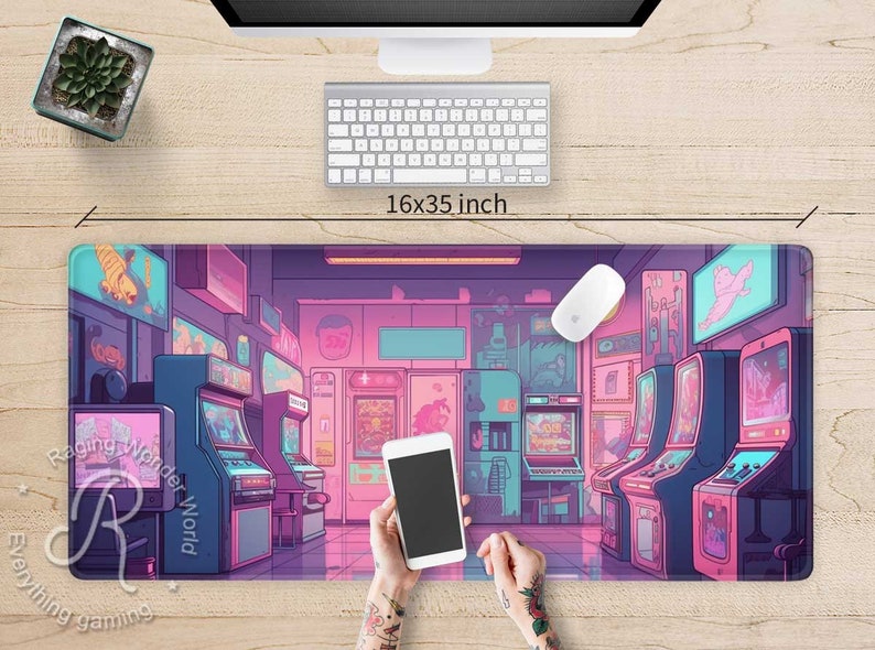 May include: A rectangular gaming mouse pad with an arcade game scene in shades of pink, purple, and blue. The pad measures 16x35 inches. A computer mouse, keyboard, and a smartphone are on the pad.