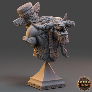 Puede incluir: Busto gris detallado de una criatura parecida a un minotauro, con cuernos, trenzas y marcas tribales. La escultura incluye una base decorativa y una estructura tipo tótem en la espalda. El logotipo de Daybreak Miniatures es visible.